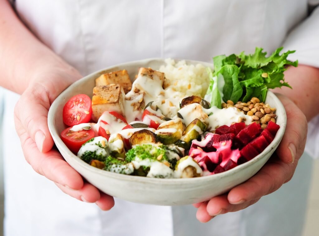 Mani che reggono una ciotola di insalata colorata con tofu, broccoli e barbabietola, esempio di pasto vario e soddisfacente